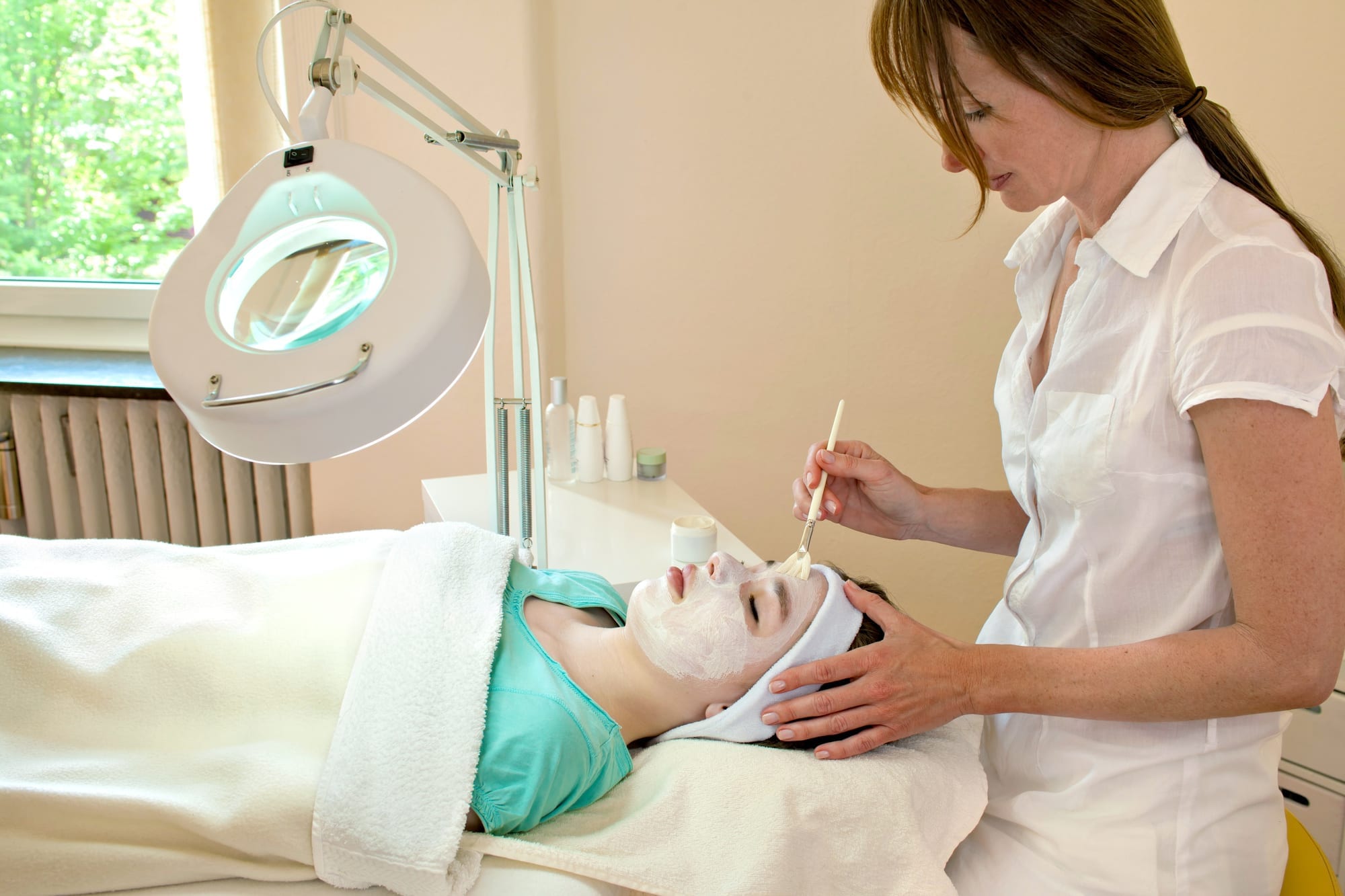 Alternative practitioner applying a chemical peel to a female patient's face in a beauty clinic