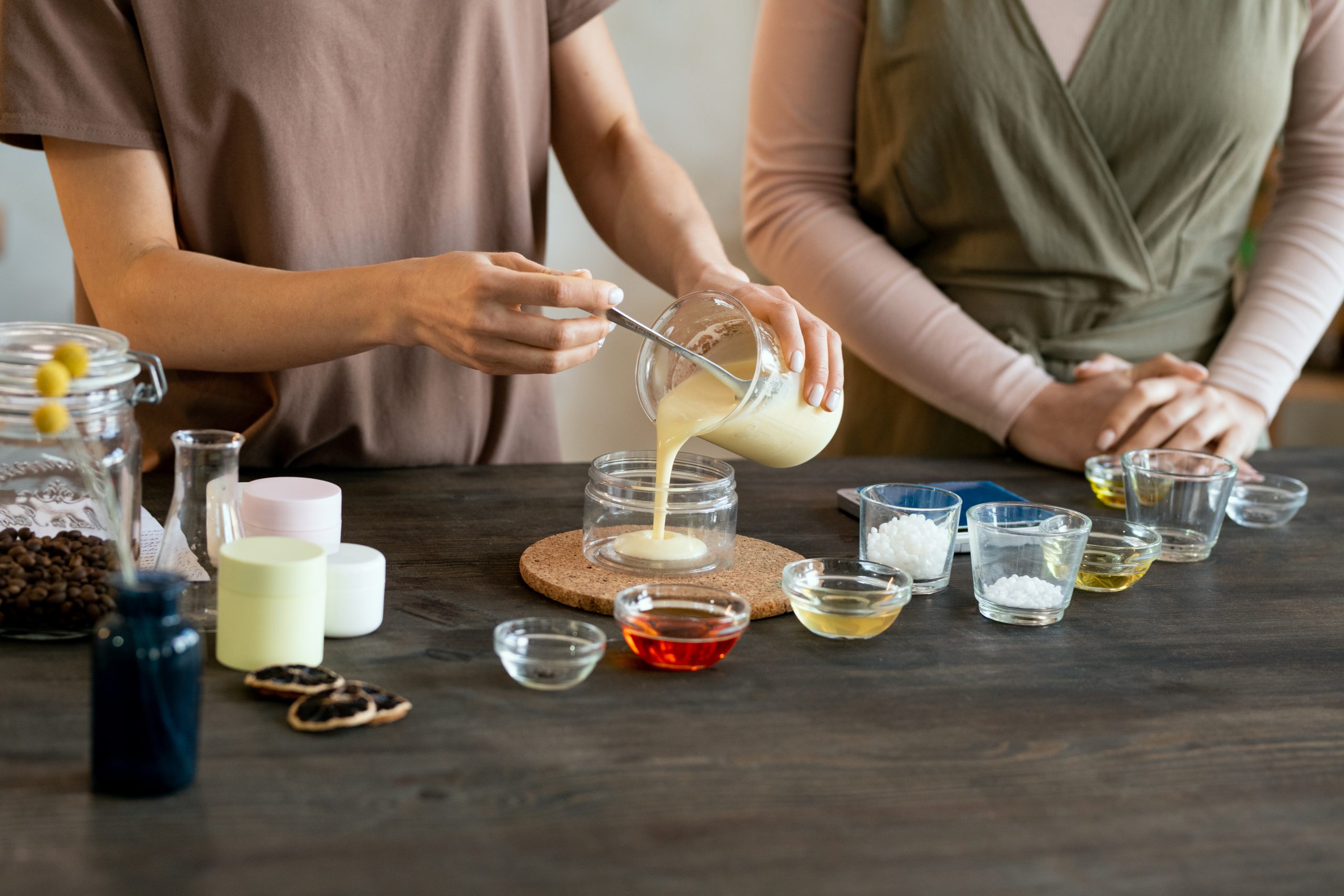 Young female putting blob of fresh handmade liquid soap mass on palm of her friend helping her with making natural handmade cosmetic products